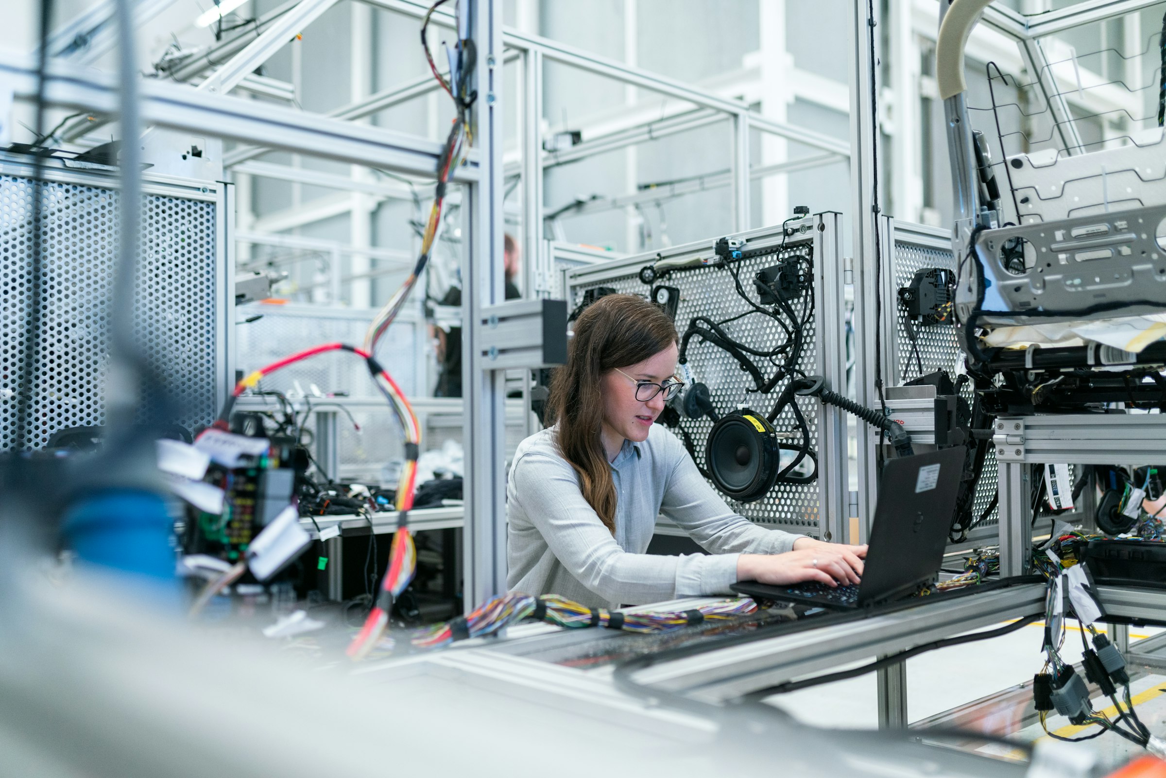 Engineer working at a laptop beside modular industrial framing, wiring harnesses and assembly components in a modern manufacturing workspace.