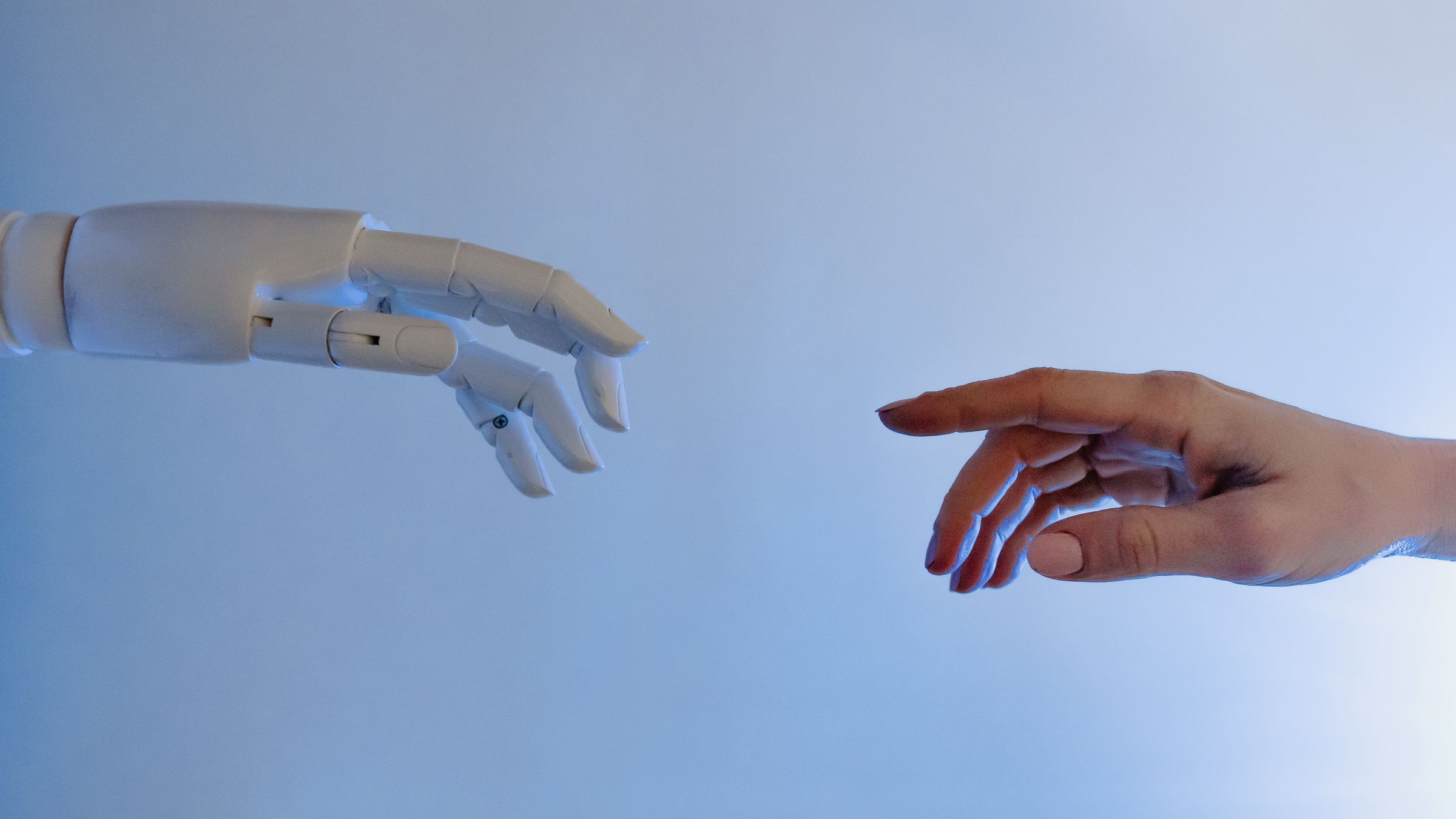 A human hand and a white robotic hand reaching toward each other against a soft blue background, symbolising practical use of technology.
