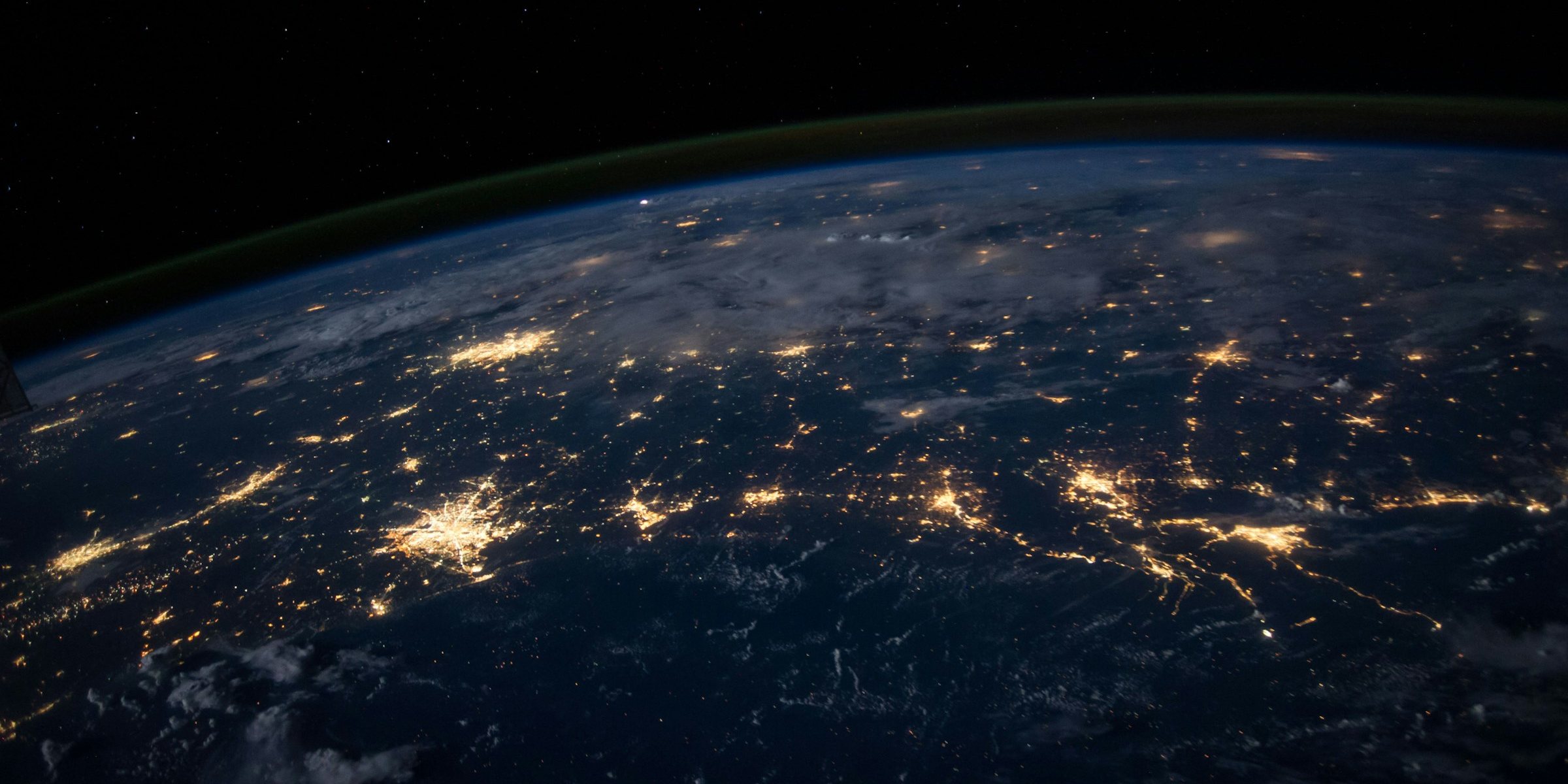 Earth at night from space, with city lights glowing across continents.
