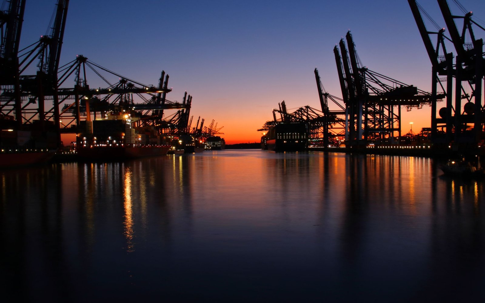 Silhouetted gantry cranes and ships at a shipping port during a vivid sunset.
